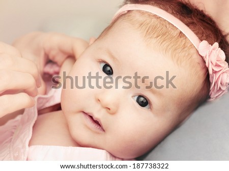 cute little baby girl with pink flower headband exploring the world while mother dressing her