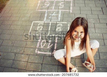 beautiful cheerful little girl playing hopscotch on playground outside