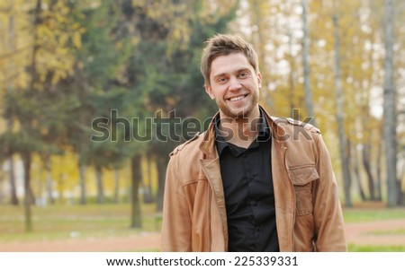 portrait of attractive happy smiling stylish young man in autumn park, outdoors background