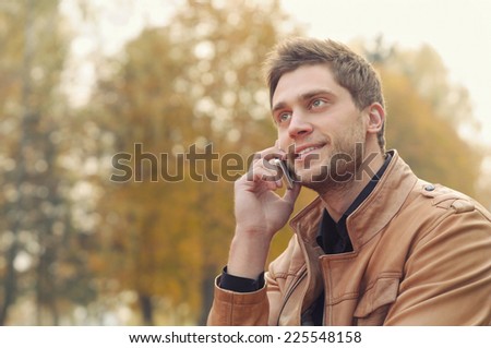portrait of beautiful attractive stylish young man speaking on the phone in autumn park, outdoors background
