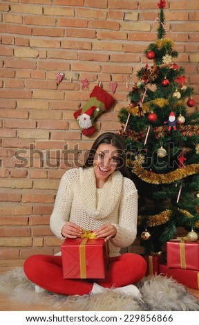 beautiful young woman with present boxes for Christmas or New Year holiday at home on brick background near Christmas tree