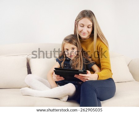 little girl with her mother using tablet device on the sofa at home, happy family, technology concept