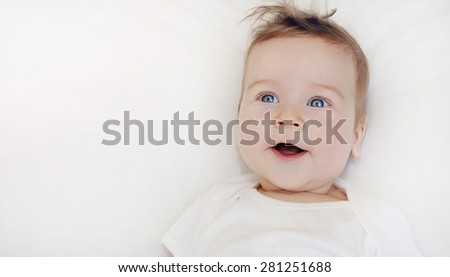 portrait of cute little happy baby boy lying on soft white pillow, happy family concept