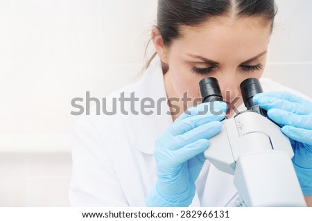young woman medical researcher looking through microscope in laboratory, medicine concept