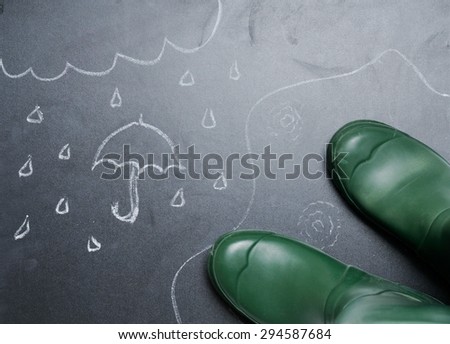 rubber boots with drawing of rainy day on the blackboard from the top view, funny lifestyle concept