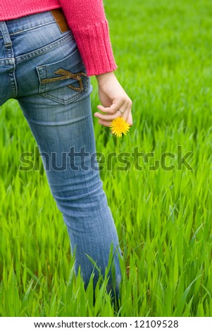 Woman from behind standing in grass, holding flower. Copy space on right. Vertical.