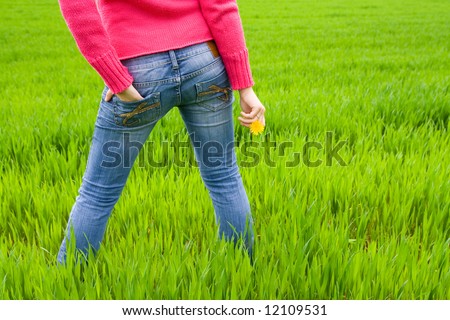 Woman from behind standing in grass, holding flower. Copy space on right. Horizontal