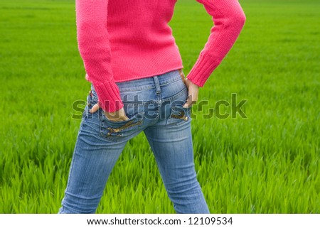 Woman from behind standing in grass with hands in pocket. Copy space. Horizontal.