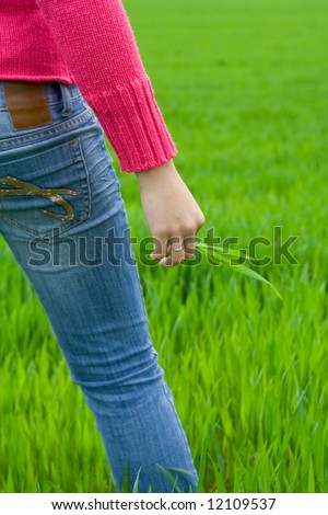 Woman from behind standing in grass, holding it. Copy space on right. Vertical.