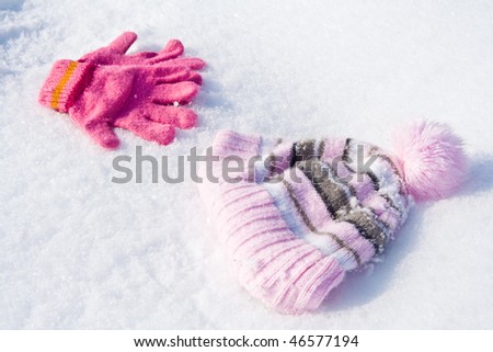 Warm female pink gloves and cap on fresh snow.