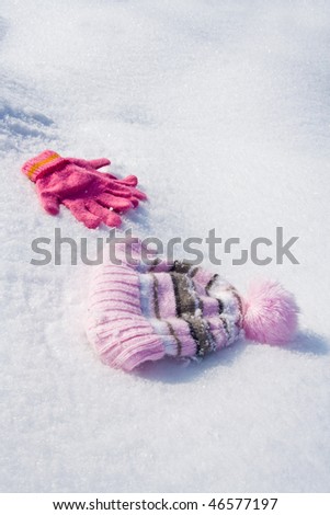 Warm female pink gloves and cap on fresh snow.
