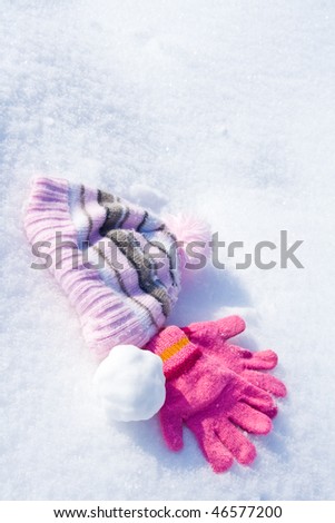 Warm female pink gloves, cap and snowball on fresh snow.