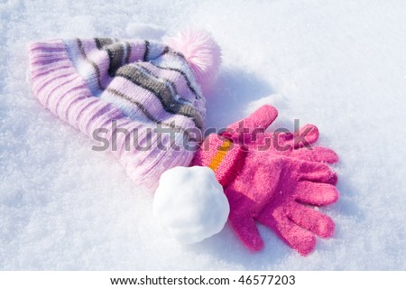 Warm female pink gloves, cap and snowball on fresh snow.