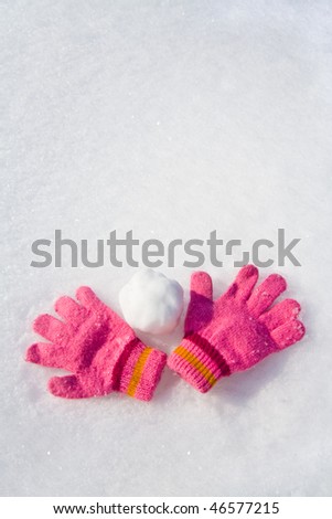 Warm female pink gloves and snowball on fresh snow.