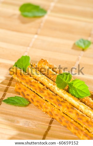 Salty sesame sticks on table cover with mint leaves.