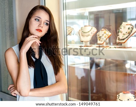 beautiful girl with long dark hair  chooses jewelry in the shop window