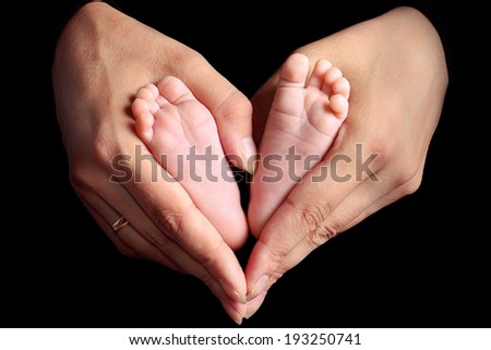legs of the newborn child in hands of careful mother,  black background