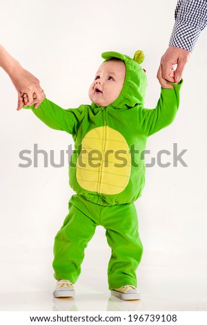 the small child in a green suit of a dragon holds parents by hands