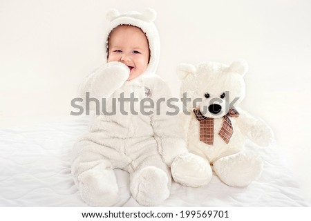 the little boy in a suit of a bear cub sits near a teddy bear on a light background