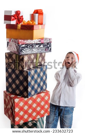surprised boy in Santa cap looking at a huge stack of gift boxes. Christmas concept.
