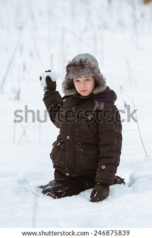 Little boy playing with snow outdoors, winter time