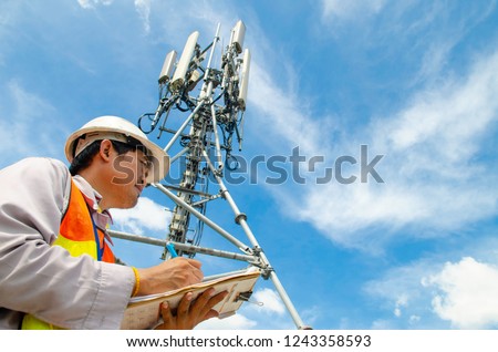Telecommunication engineer writing on notepad at tower site.Technician record data of maintenance to checklist.