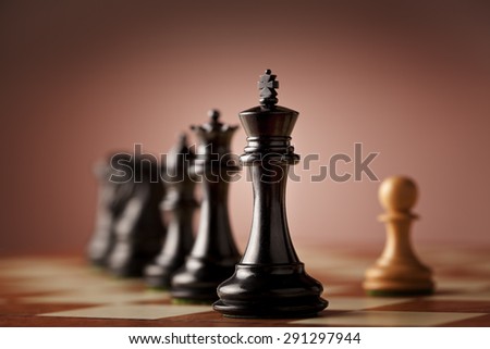 A line of luxurious chess pieces carved in genuine ebony wood facing a single white pawn made of natural boxwood standing on elm burl and bird\'s eye maple superior traditional chessboard
