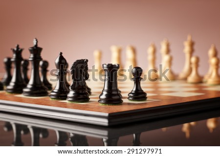 Black rook in focus with other black luxurious chess pieces on a wooden chessboard before the game