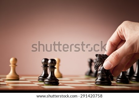 Male hand holding the black chess knight in focus at the end of a chess game