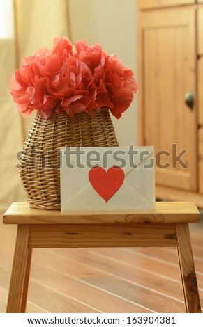 Vase basket with red tissue paper flower-pom pom and love letter with red heart sticker on small wooden step stool