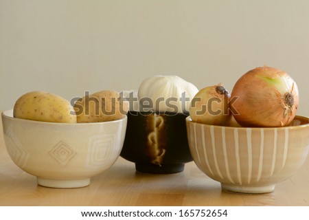 Close up of potatoes, garlics, and onions in three separate small bowls on the table