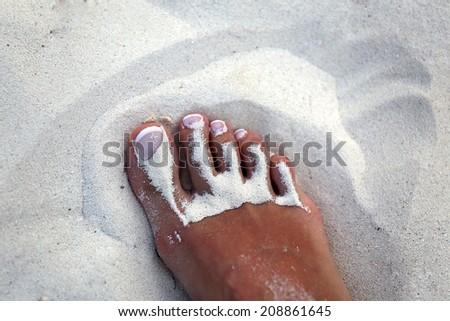 foot girl with white pedicure in the sand