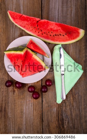 slices of watermelon on the plate next with plums on a wooden background