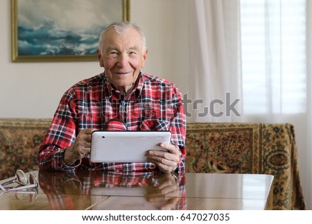 Handsome senior man using digital tablet sitting at the table in the living room