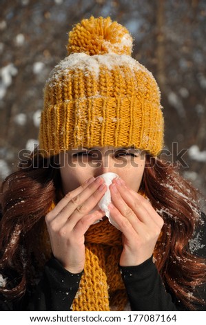 Woman sneezing into tissue, winter outdoor portrait