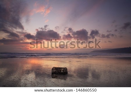 Morning after the storm. As the morning light breaks over the sea reflecting in the golden sand a lobster pot sits quietly having been torn from it\'s mooring\'s on the sea bed.