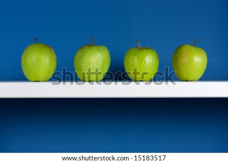 Four green apple on white bookcase