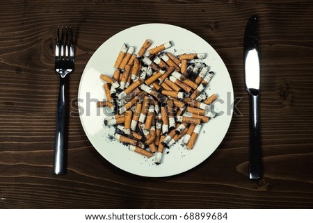 Plate with cigarettes stubs with cutlery on wood desk