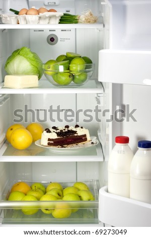 Open refrigerator full with some kinds of food - chocolate cake, lime, apples, eggs, milk