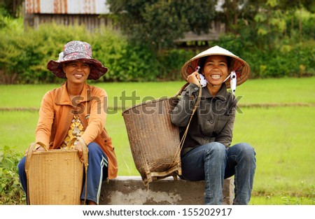 DAKLAK, VIET NAM- SEPTEMBER 5. Two woman wear hat , carry papoose ( gui) with smile on face, sit and wait on roadside at golden light evening. September 5, 2012
