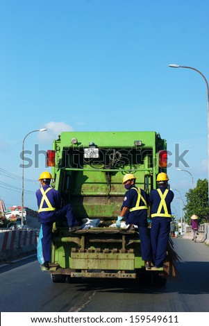 LONG AN, VIET NAM- JUNE 28: Three sanitation stading on dump truck which moving on street on working day, Long An, Viet Nam, June 28, 2013