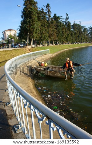 DA LAT, VIET NAM- DEC 29: Vietnamese sanitation worker working on Xuan Huong lake, he\'s  sit on boat and pick up trash from surface water to clean up the lake in Dalat, Vietnam on Dec 29, 2013