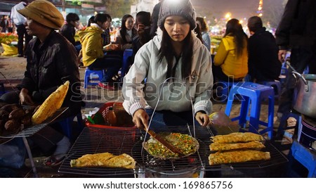 DA LAT, VIET NAM- DEC 29: Vietnamese street food vendor grill baked girdle cake- one of eating street, people at oudoor market in cold night- lifestyle of young person in Dalat, Vietnam on Dec 29,2013