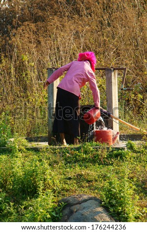 DAKLAK, VIETNAM- FEB 6: People  scoop water from water well by bucker, woman wear colorful clothing, the well at meadow in Vietnamese countryside, Viet Nam, Feb 6, 2014