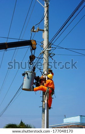 BINH THUAN, VIETNAM- JAN 23: Two electrician repair system of electric wire, they wear safety working clothing, climb and work on electric pole with team under blue sky, Viet Nam, Jan 23, 2014