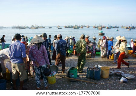 PHAN THIET- VIETNAM- JAN 21: Crowed atmosphere at outdoor seafood market on beach, people trader fishing product in morning, boat on water, man vs woman buy and sell fresh food, Viet Nam, Jan 21, 2014