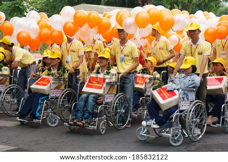 HO CHI MINH, VIET NAM- APRIL 6: Group of invalid people on wheelchair in a row with young volunteer on street, begin charitable activity event for handicapped community, Vietnam, April 6, 2014