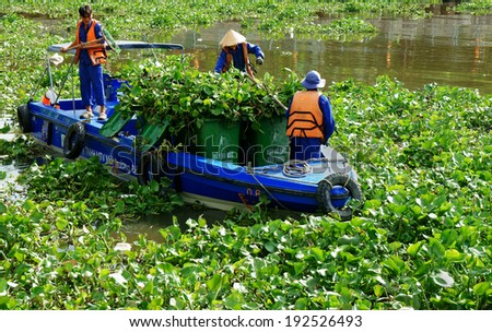 HO CHI MINH CITY, VIETNAM- MAY 13: Group of Vietnamese sanitation worker working on Nhieu Loc canal, three people in uniform and life jaclet try to take water hyacinth on boat, Viet Nam, May 13, 2014