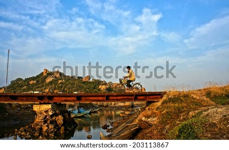 BINH THUAN, VIET NAM- JAN 23: Impression landscape of Vietnamese countryside with mountain chain, rock, stone, old man riding bike on bridge cross river under blue sky, Vietnam, Jan 23, 2014