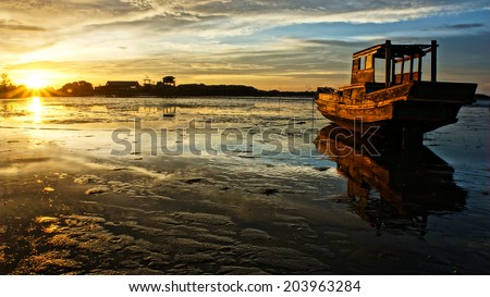Abstract landscape of sea when sunset, tide going out, sun go down, sunbeam shine on wooden fishing boat that reflect on surface water of beach, colorful sky at evening scene